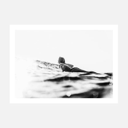 A black and white photo print of a surfer paddling in the ocean.