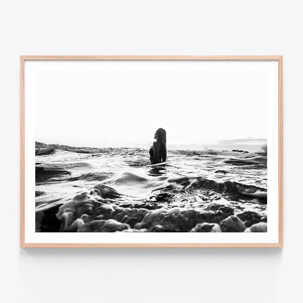 A framed black and white photograph of a girl swimming in the ocean with waves around her.