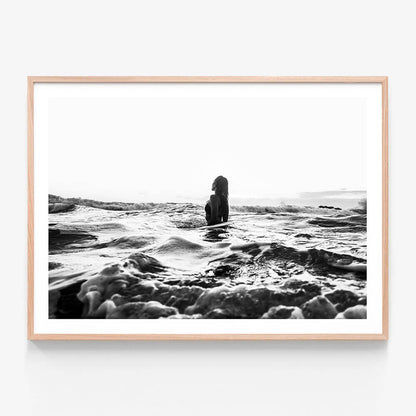 A framed black and white photograph of a girl swimming in the ocean with waves around her.