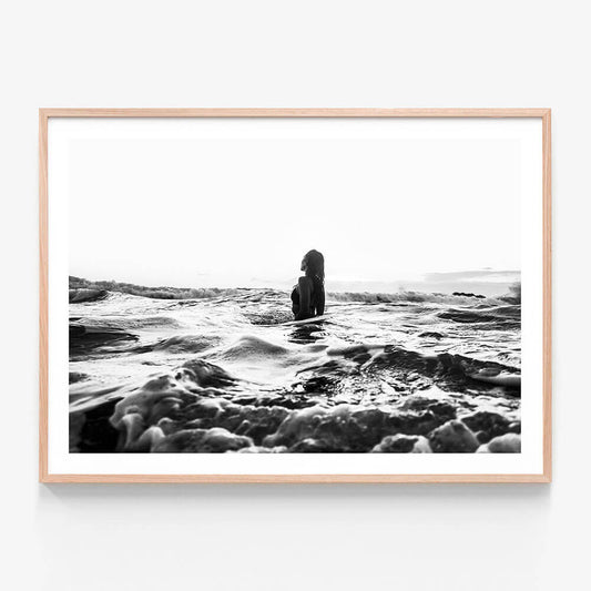 A framed black and white photograph of a girl swimming in the ocean with waves around her.