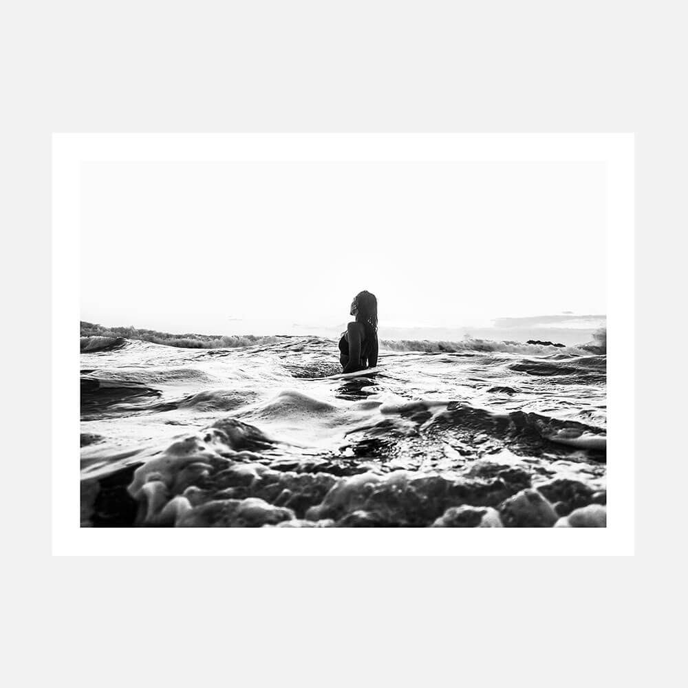 A black and white photography poster print of a girl standing in the ocean with waves around her.