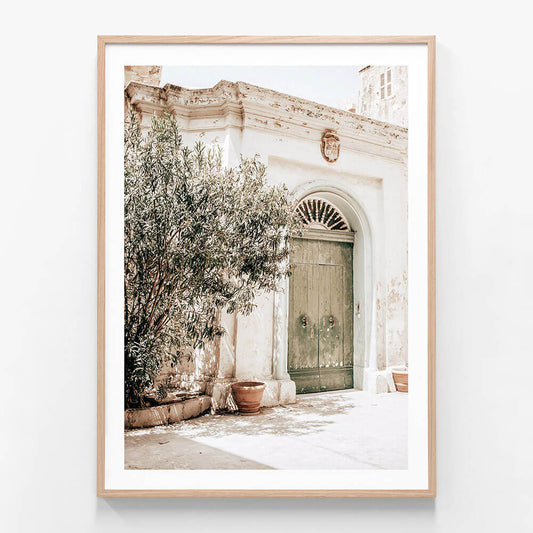 A framed photo art print of a old town street with an old door and a tree.