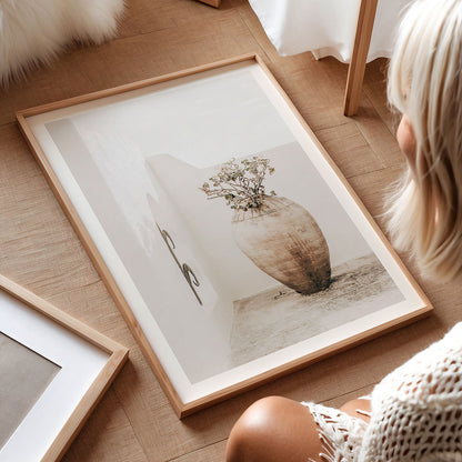 Framed photography print of a vase and scissors on a wooden floor with a person partially visible.