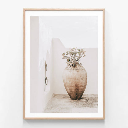 A framed artwork featuring a large earthenware vase with a dried plant arrangement, placed against a neutral background.