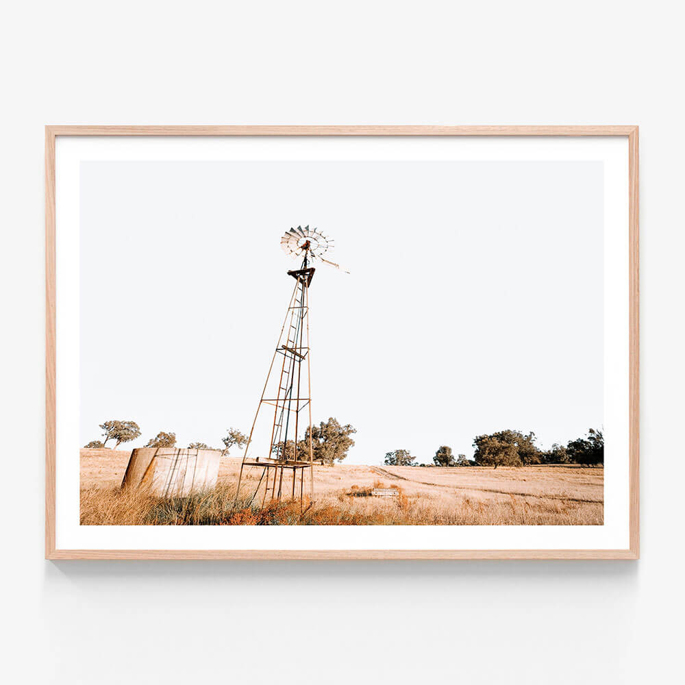 A framed photo print of an old windmill in a field, with a predominantly beige and brown color palette, typical of a Australian farming scene.