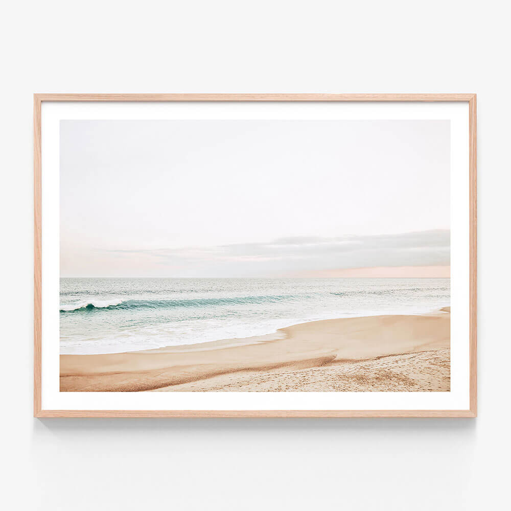 A pastel-colored photograph of a coastal scene with a beach and ocean waves in the background. Framed wall art print