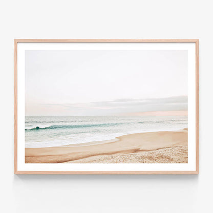A pastel-colored photograph of a coastal scene with a beach and ocean waves in the background. Framed wall art print