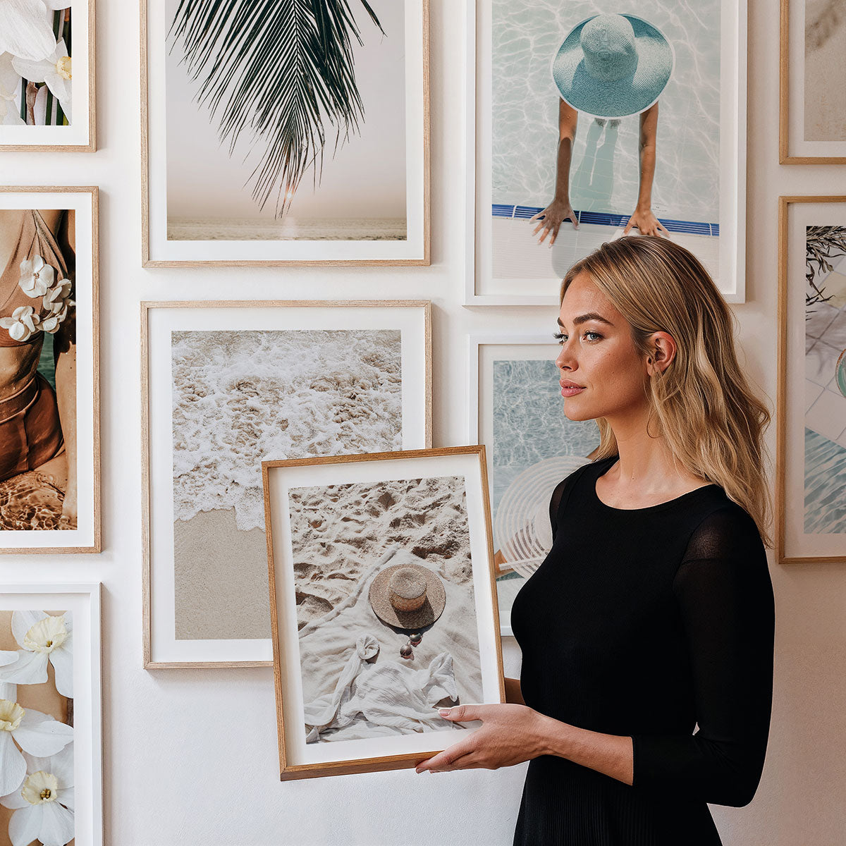 Woman holding a framed print in front of a wall of framed photographic wall art.