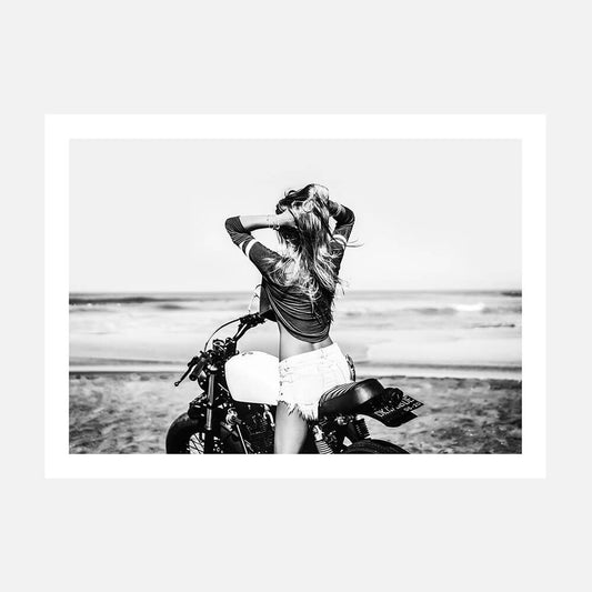 This art print features a striking black and white photograph capturing a vivid beach scene. A woman is seen sitting on a motorcycle with a backdrop of the ocean and sand dunes.
