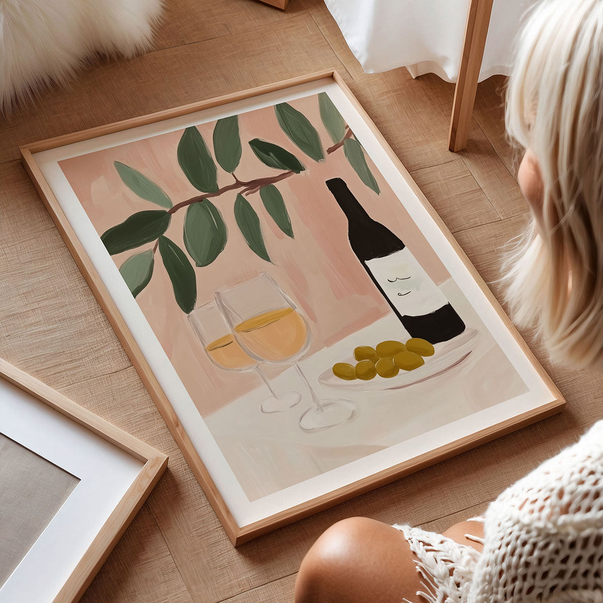 Framed still life artwork of a bottle of wine, glasses, and olives on a wooden floor.