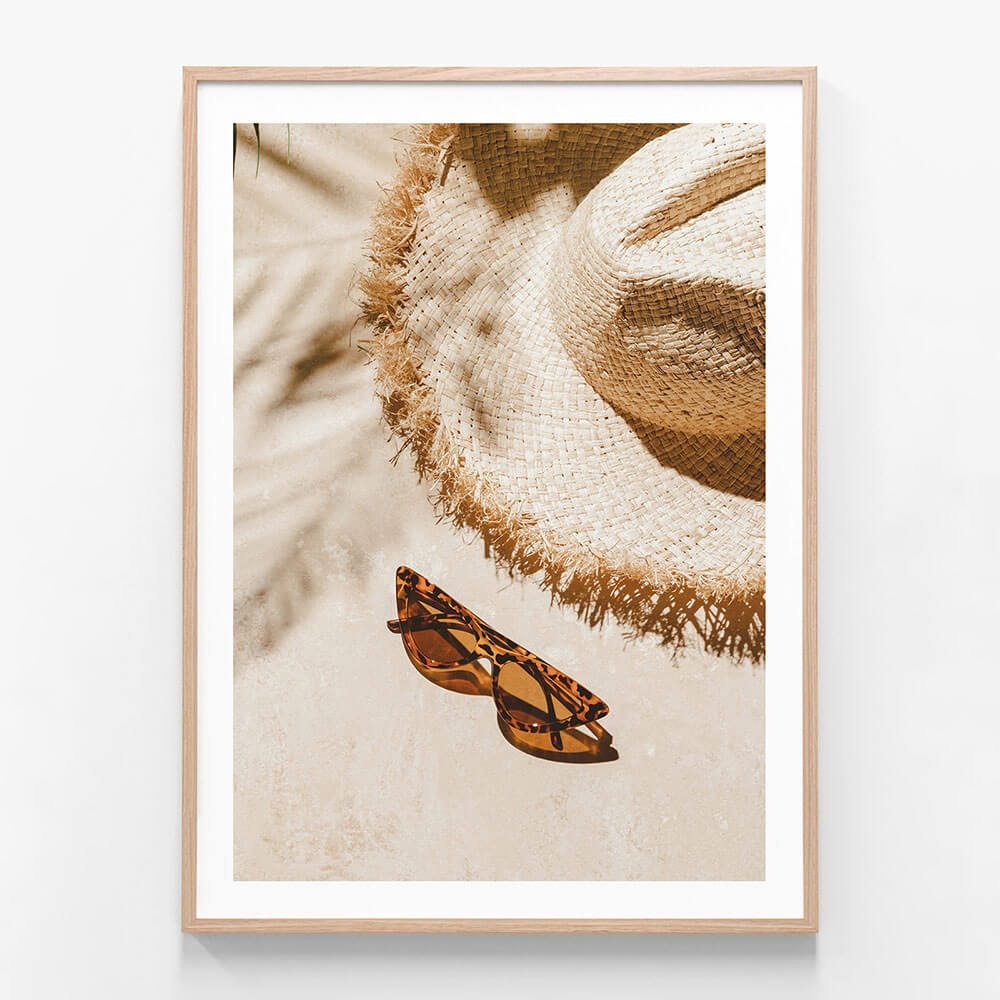 A framed photo wall art print featuring a sun hat and sun glasses on the beach on a sunny day