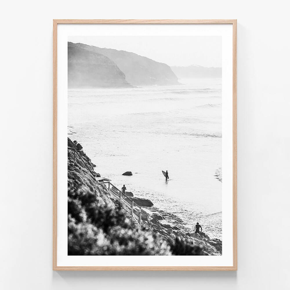 A framed black and white photograph of surfers in the ocean at Bells beach with a coastal landscape in the background.