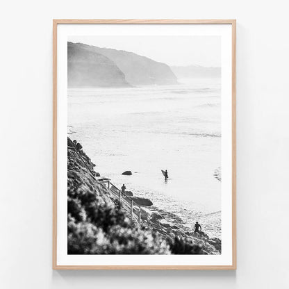 A framed black and white photograph of surfers in the ocean at Bells beach with a coastal landscape in the background.