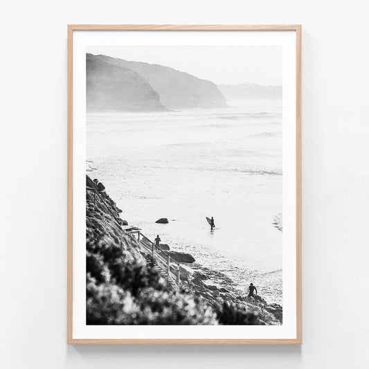 A framed black and white photograph of surfers in the ocean at Bells beach with a coastal landscape in the background.
