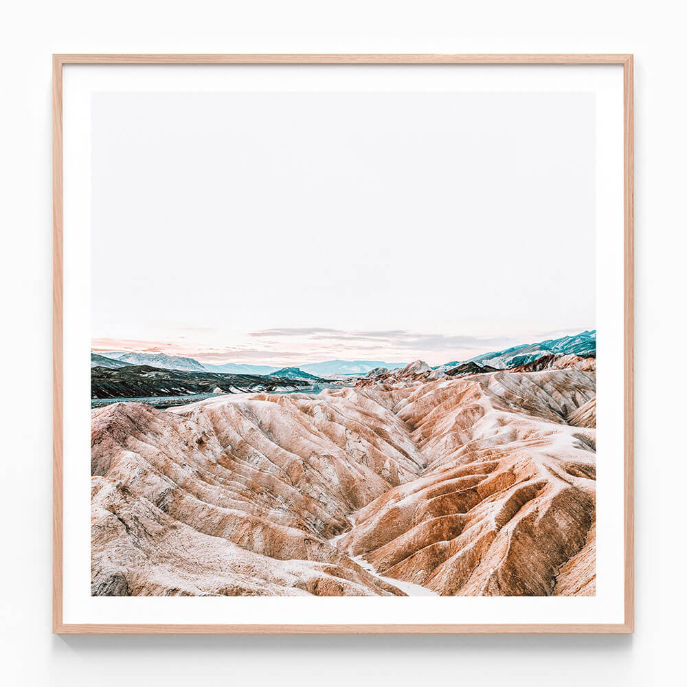 A framed landscape photo of eroded badlands with hues of brown, beige, and blue, likely taken in a desert region.