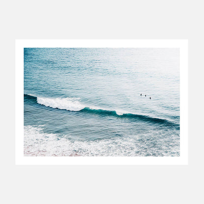 A photo featuring a coastal scene with gentle waves and three surfers in the distance.