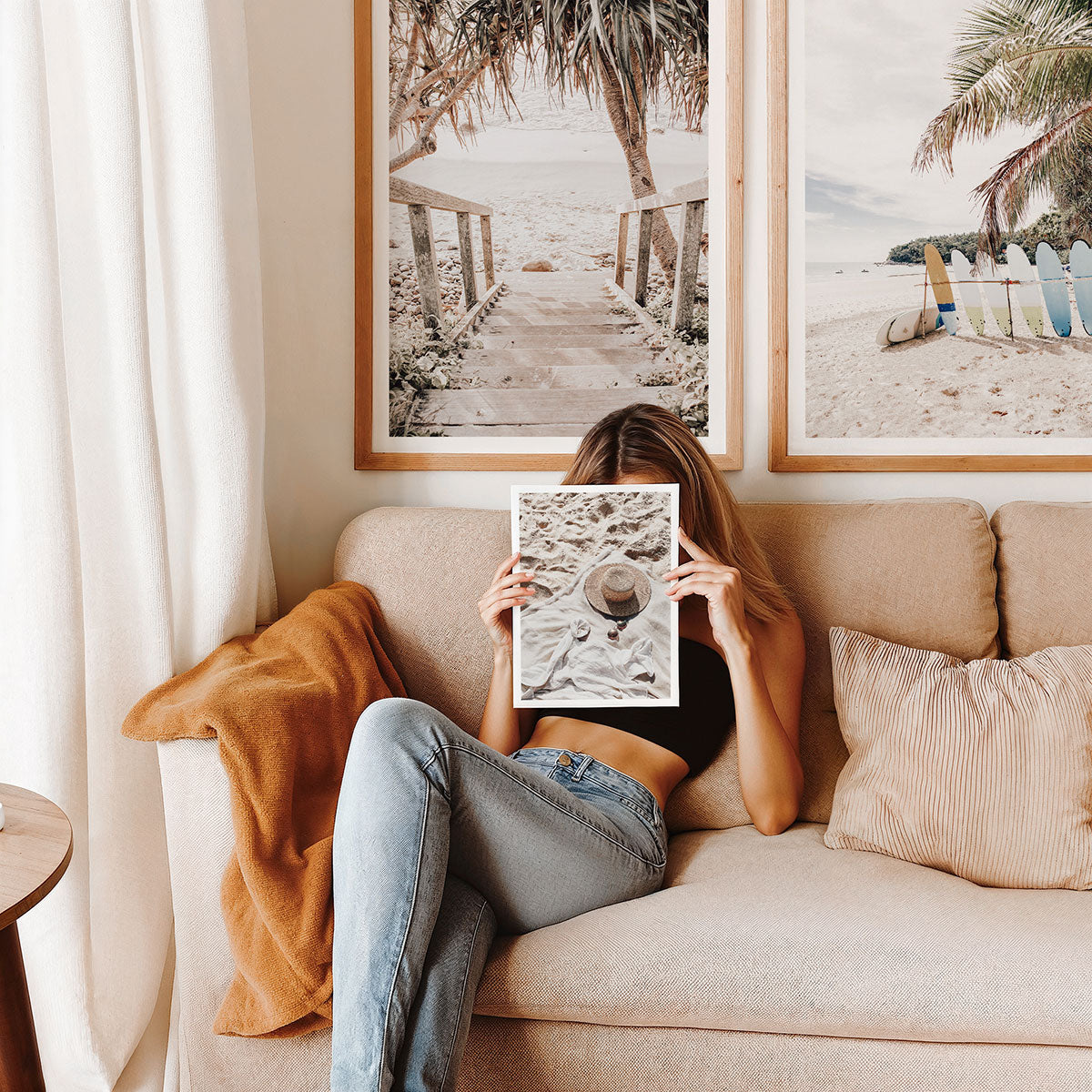 Person sitting on a couch holding beach themed wall art, framed prints in the background of a tropical beach.
