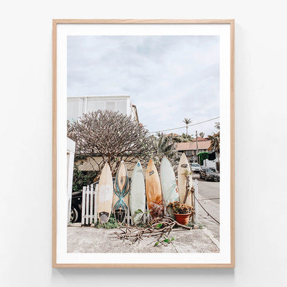 A photo wall art print featuring surfboards lines up against a fence in a beach street