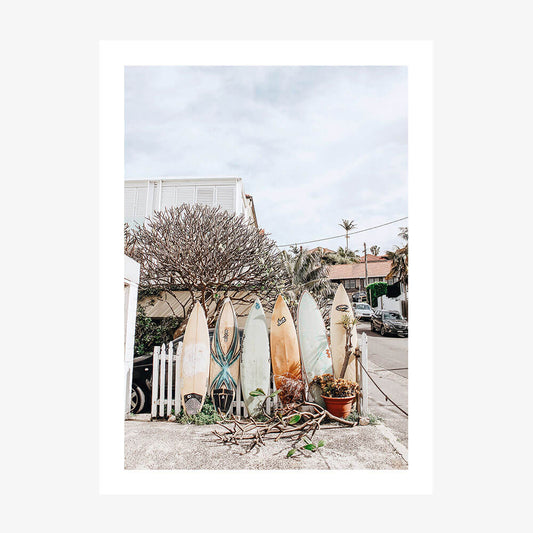 A photo wall art print featuring surfboards lined up on a street near the beach